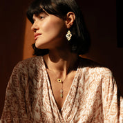 Woman wearing  gold platted embrace  earrings with a warm light background