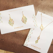 Gold jewelry set on 'Embrace' branded cards against a brown textured background