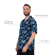 A man wearing a navy blue short-sleeve scrub top with a white floral pattern, shown against a plain white background with text callouts highlighting features like durable wooden buttons, breathable cotton, and a loose fit.