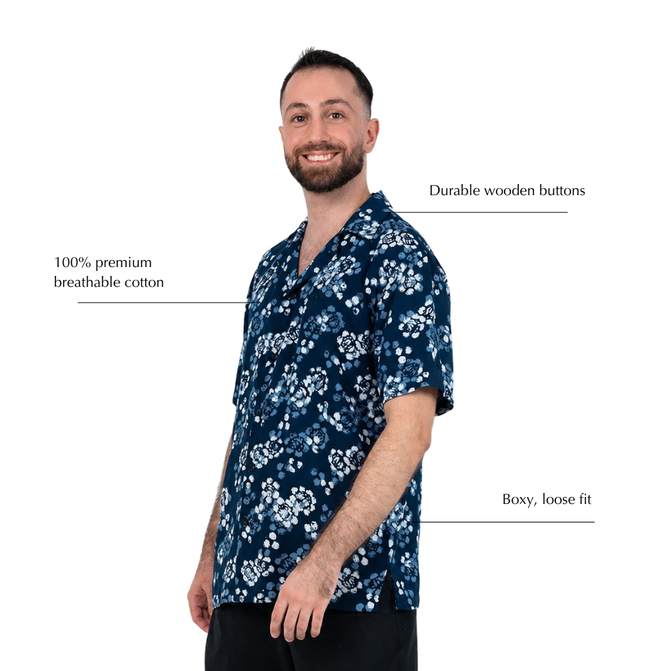 A man wearing a navy blue short-sleeve scrub top with a white floral pattern, shown against a plain white background with text callouts highlighting features like durable wooden buttons, breathable cotton, and a loose fit.