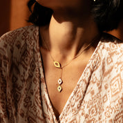 Necklace with geometric pendants worn by a person in a patterned garment.