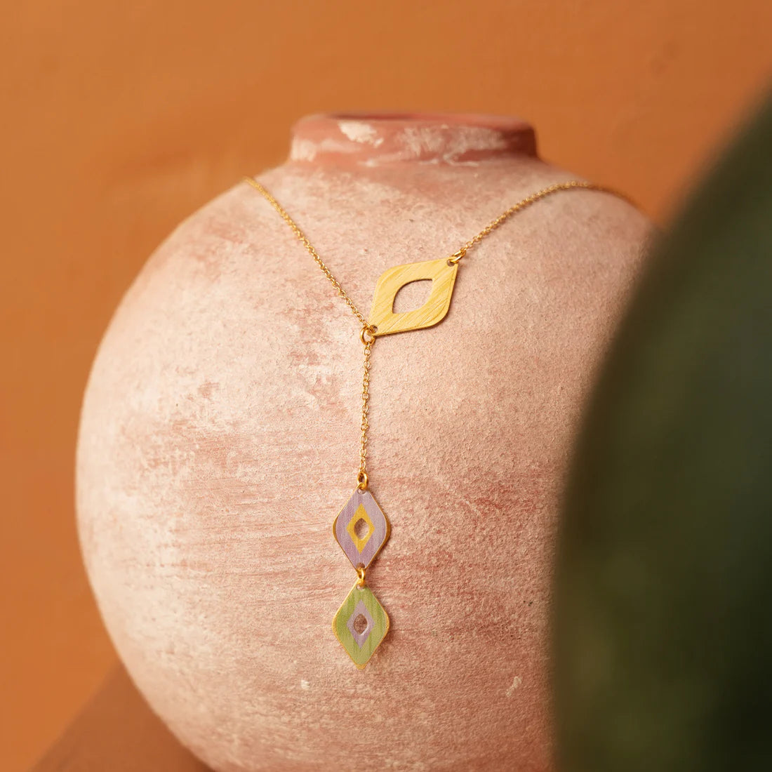 Gold necklace with geometric pendants on a textured pink surface against an orange background