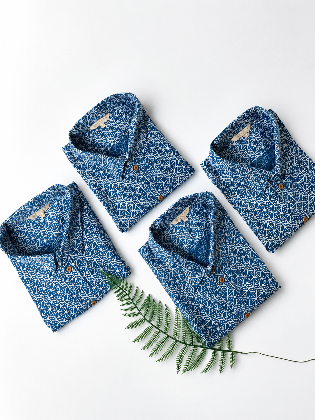 Folded blue patterned shirts on a white background with a green leaf.
