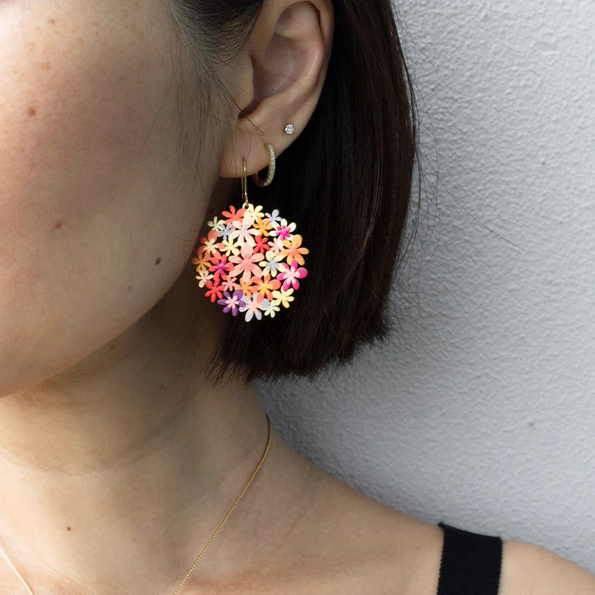 Close-up of a person wearing colorful orangebouquet earrings against a neutral background