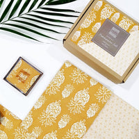 a flatlay photo of homeware gift set in the pattern golden pineapple made of batik with reversible coasters and placemats