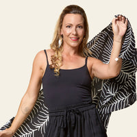 a woman posing in front of a neutral background happily with a batik scarf in the pattern black fern wrapped around her