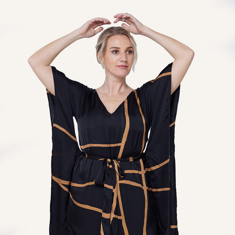 a model posing in a caftan dress made of batik in the pattern black ecru against a neutral background