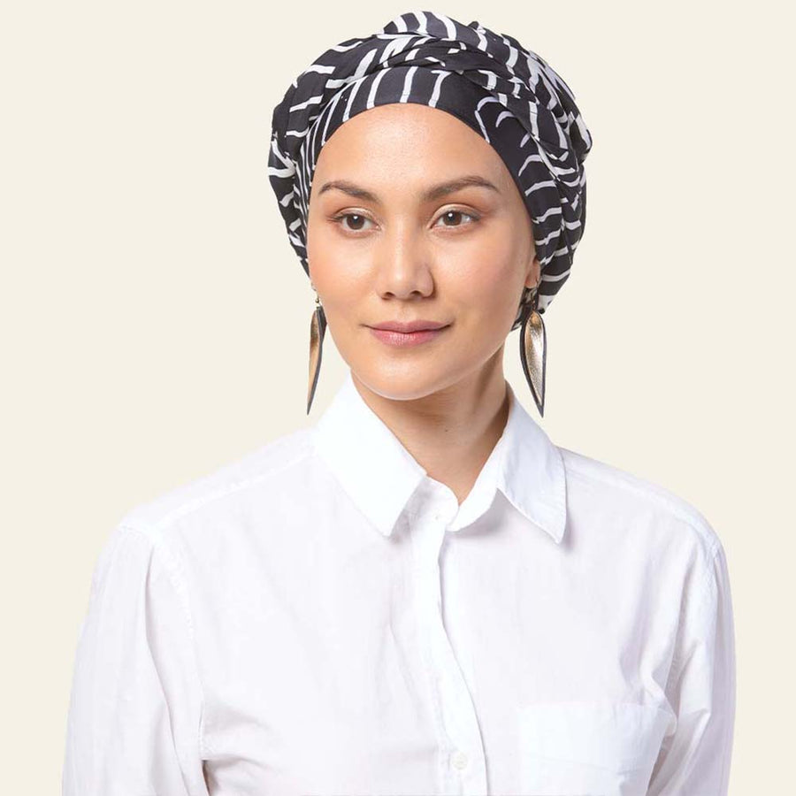 a model posing in front of a neutral background in a batik scarf in the pattern black fern
