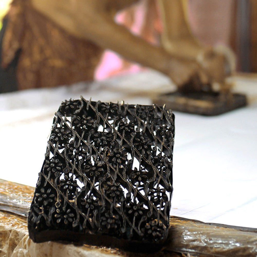 a photo of a batik block with an artisan blocking in batik in the back