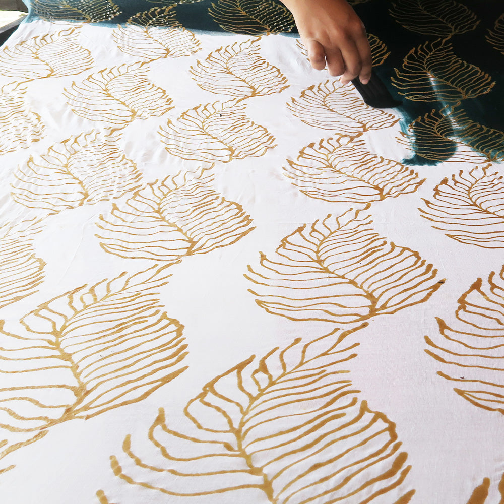 an artisan in the process of coloring batik in the pattern fern