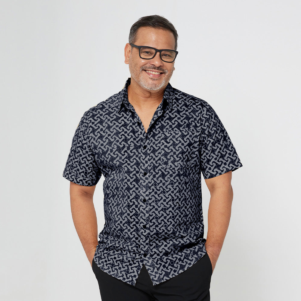 A man standing in front of white backdrop wearing black & grey batik motif in Arabesque. The model is facing front