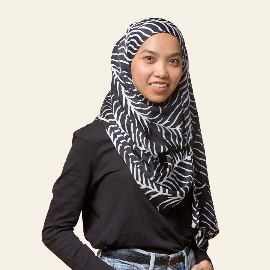 a woman posing in front of a neutral background while wearing a batik headscarf in the pattern black fern against a neutral background