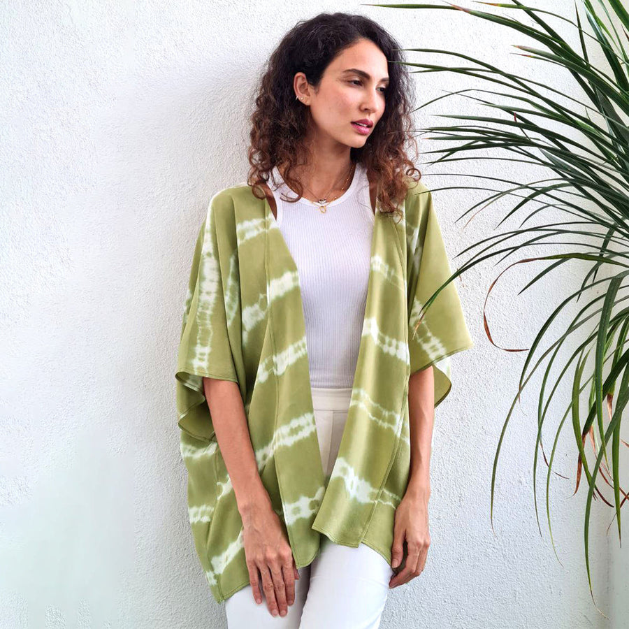Woman dreaming by tropical plant wearing short Shibori Kimono in Olive handcrafted batik print, made in Malaysia.