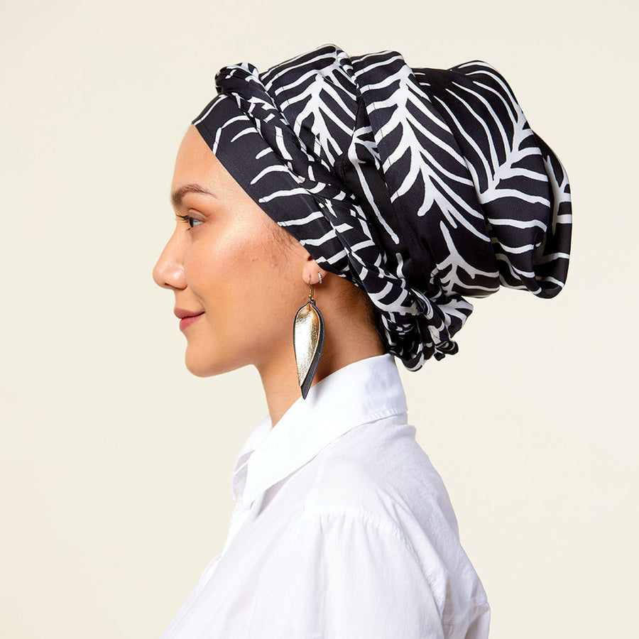 a woman posing while wearing a batik scarf in the pattern black fern in front of a neutral background accompanied by a large earring